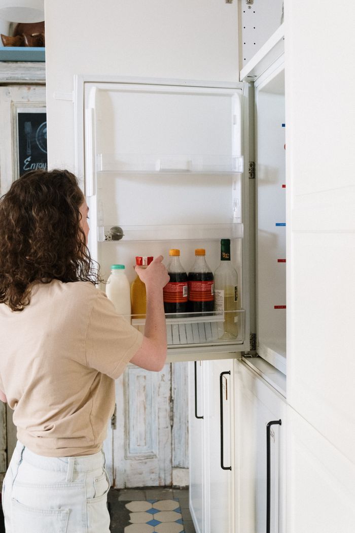 why-choose-us-03 Woman with curly hair reaches for a drink in the kitchen fridge.