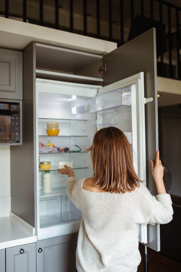 about-02 A woman reaches into a refrigerator in a contemporary kitchen, creating a lifestyle moment.