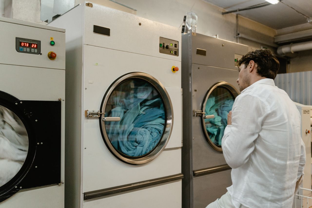 services-05 A man wearing a white shirt uses industrial washing machines in a public launderette.