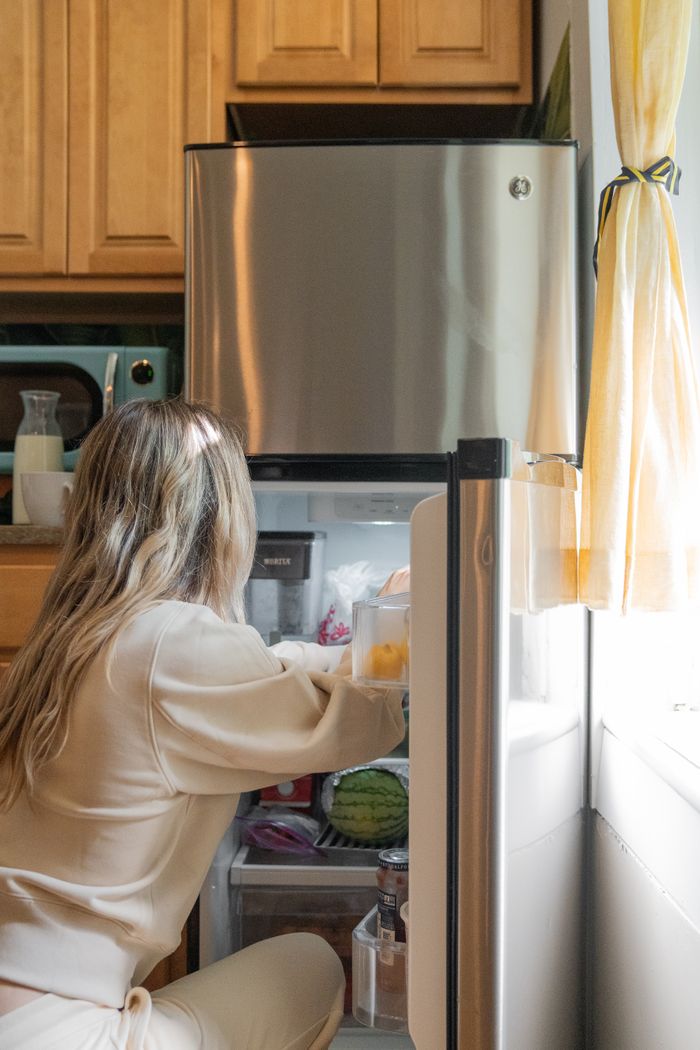 why-choose-us-02 A woman reaches inside a refrigerator in a sunlit kitchen, arranging groceries.
